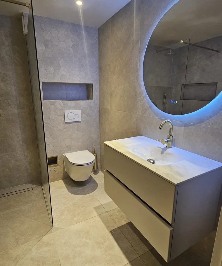 Zwevend badmeubel met wastafel en ronde verlichte spiegel, naast een hangtoilet en inloopdouche