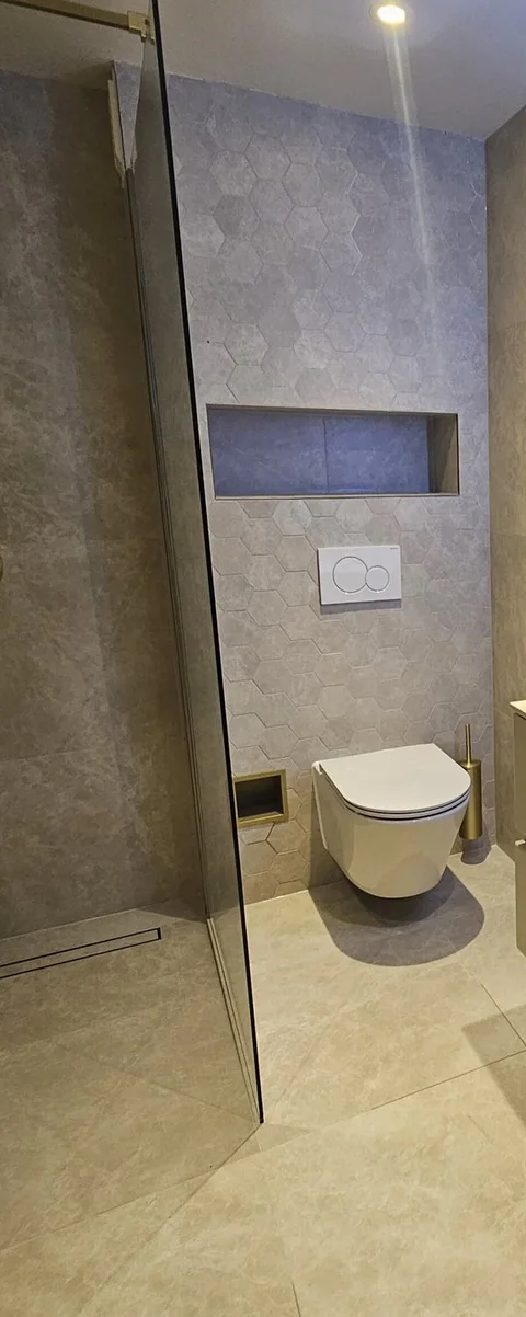 Heldere glazen douchewand met dun profiel, naast een hangtoilet