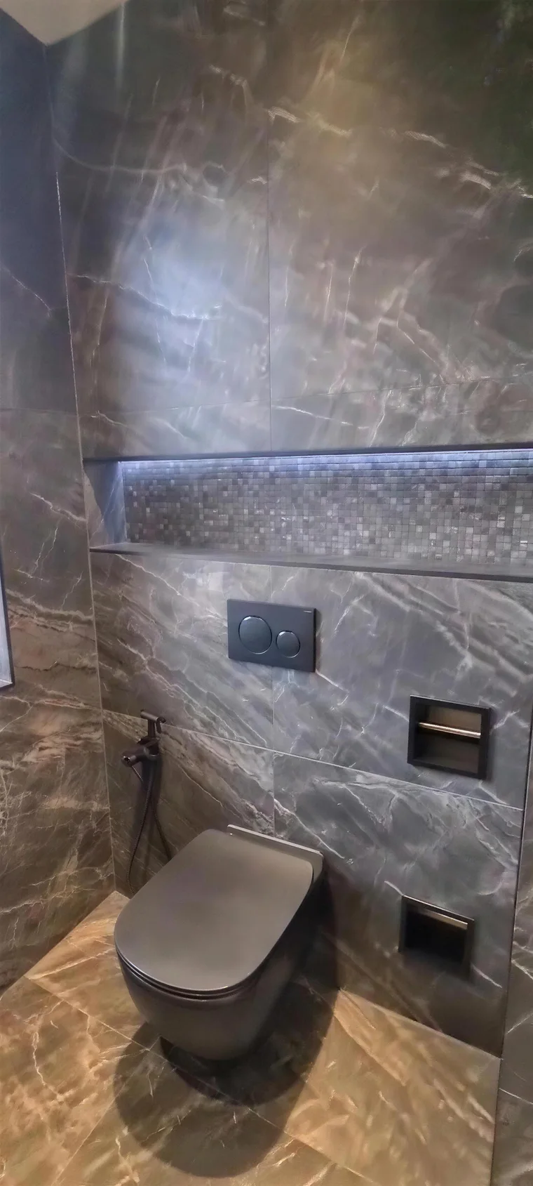Verlichte nis met mozaïek in de wand boven een hangtoilet
