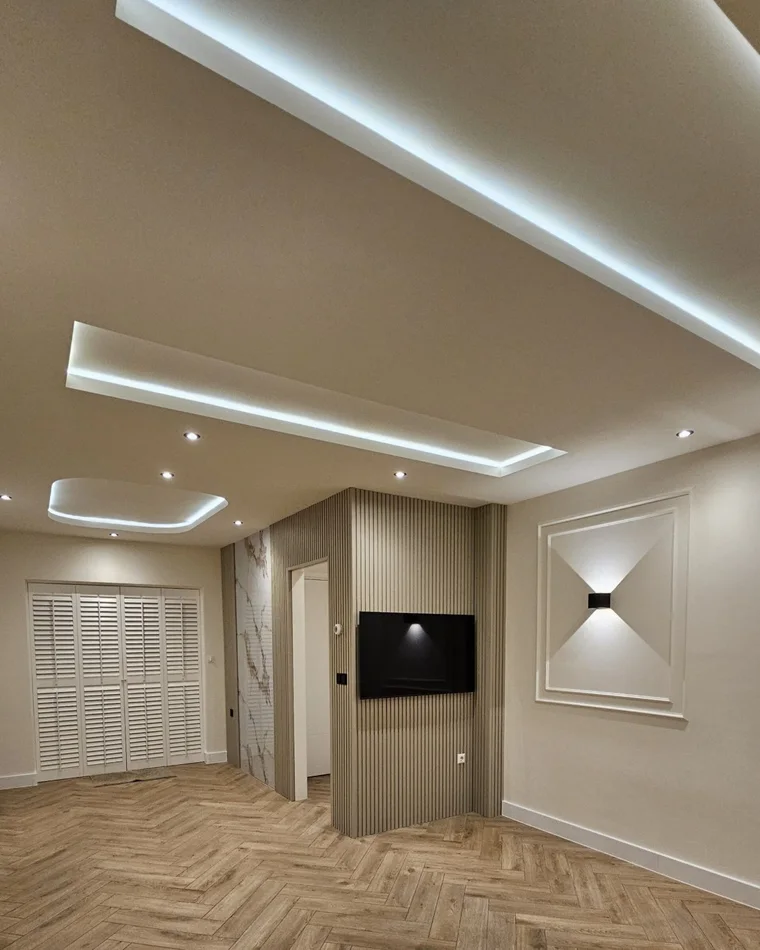 Woonkamer met verlaagd plafond en indirecte ledlijn, visgraatvloer en wandpanelen